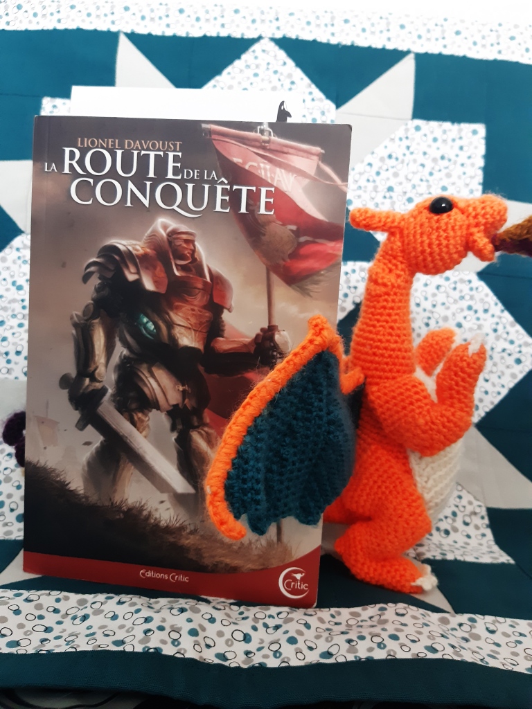 Livre La Route de la Conquête posé à côté d'un Dragon orange au crochet. 